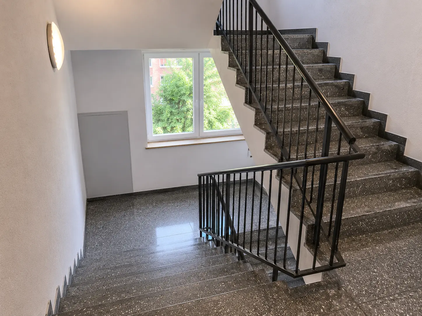 Treppenhaus eines Wohngebäudes mit dunklen Granitstufen, Handlauf und Fenster
