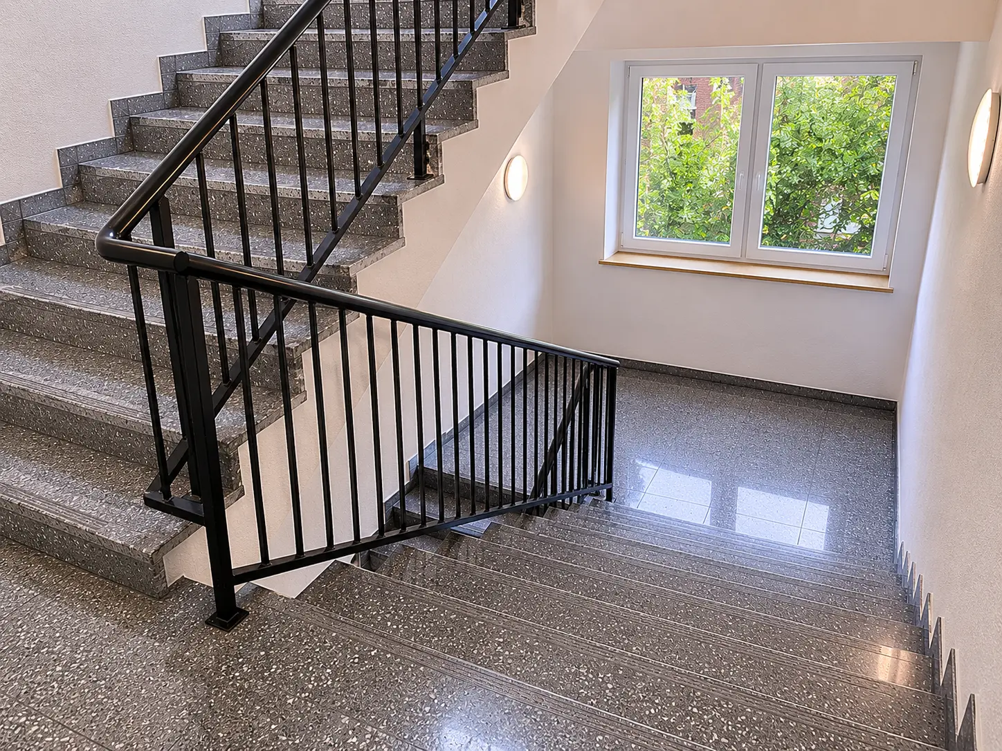 Frisch gereinigtes Treppenhaus mit glänzenden Terrazzostufen und dunklem Geländer