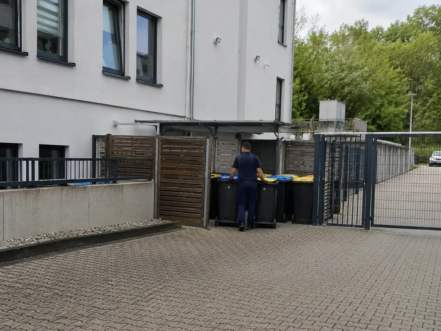 Mitarbeiter schiebt die Mülltonnen am überdachten Müllstandplatz einer Wohnanlage zurecht