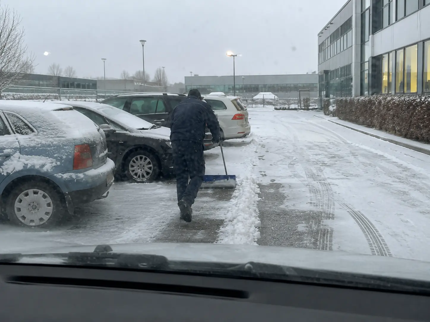 Mitarbeiter schiebt den Schnee von den Stellplätzen eines Firmenparkplatzes vor dem Bürogebäude