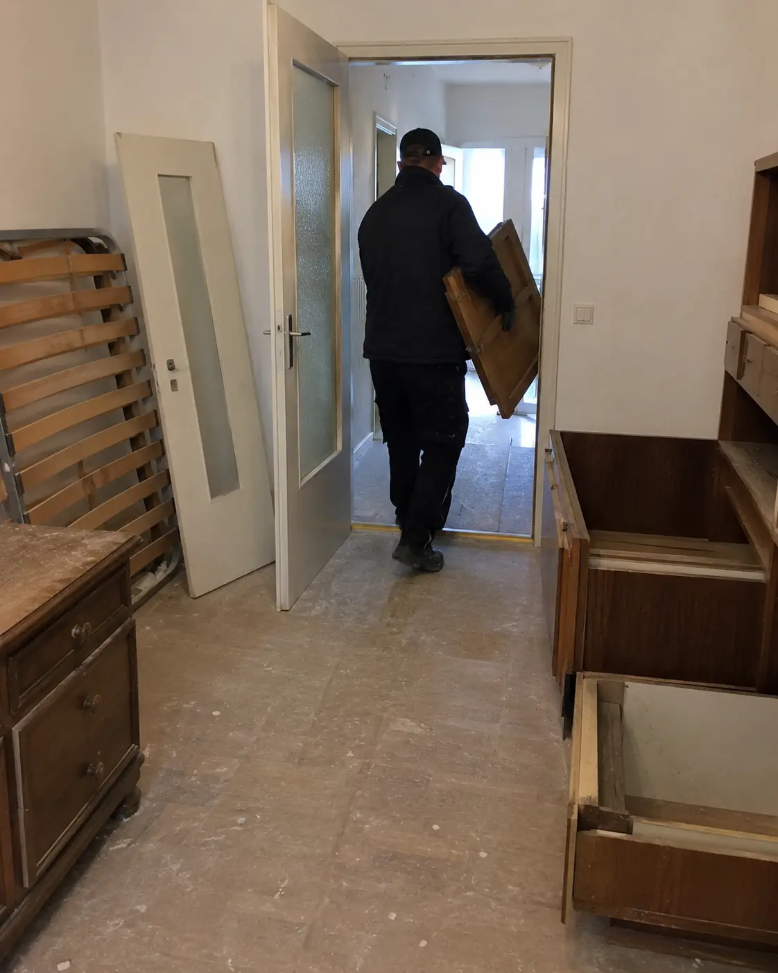 Mitarbeiter trägt ein Schrankteil aus einer Wohnung, im Raum stehen ausgeräumte Möbel und ein Lattenrost
