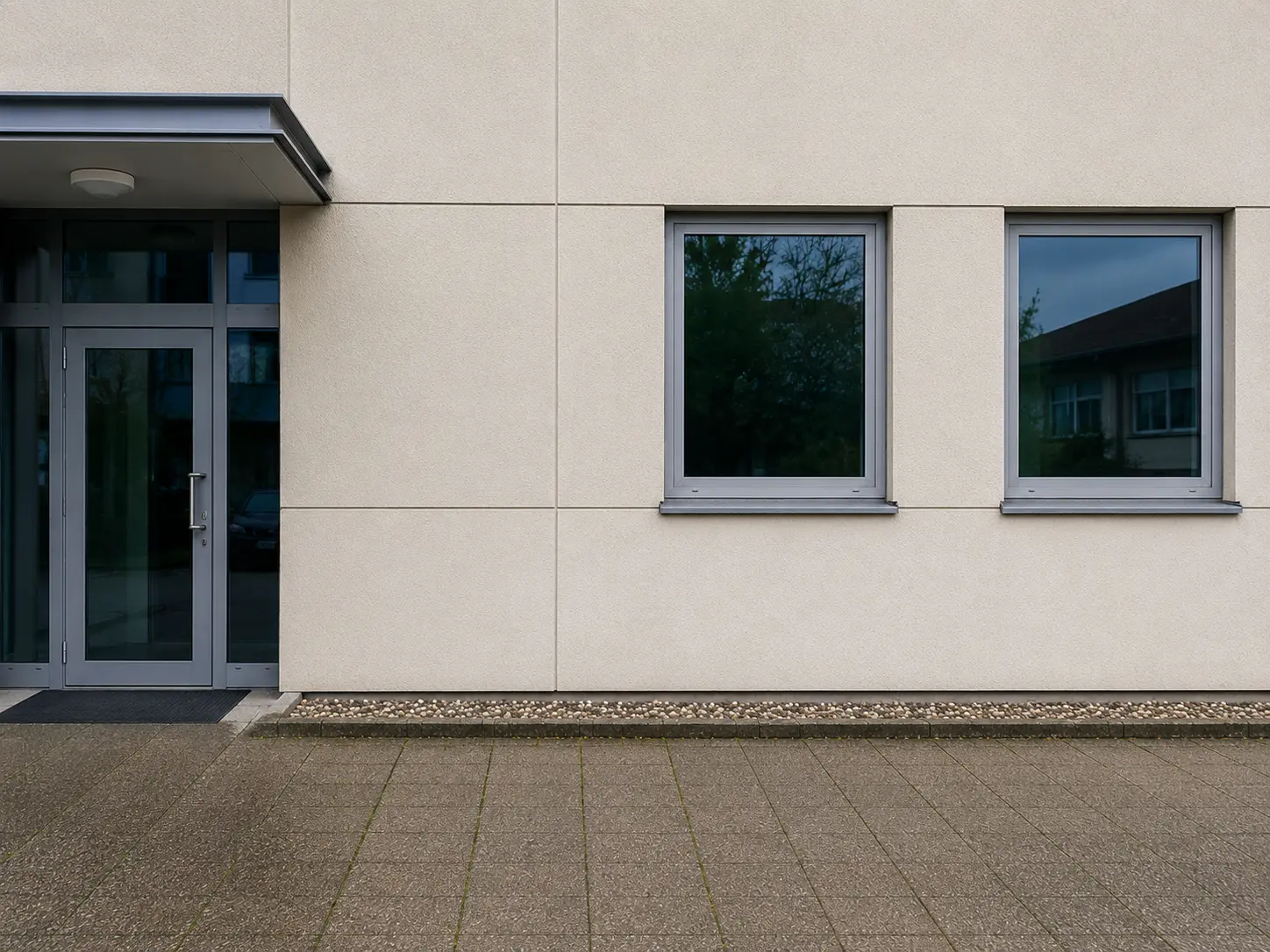 Heller Gewerbeingang mit Glastür, Vordach und sauberer Putzfassade