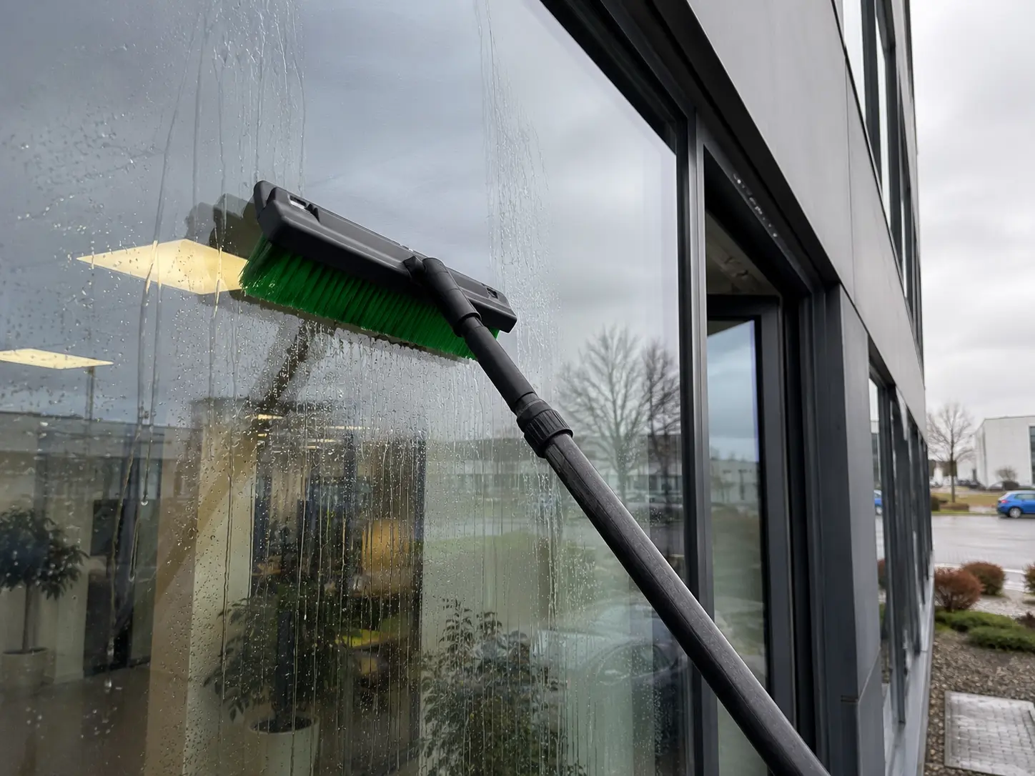 Einwascher an der Teleskopstange auf der nassen Glasfassade eines Bürogebäudes